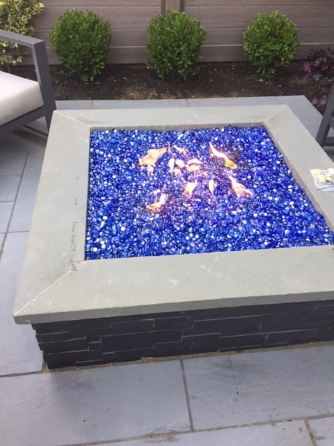 Norstone Aksent Modern Stone Cladding in Ebony Color on a gas firepit with bright blue glass media